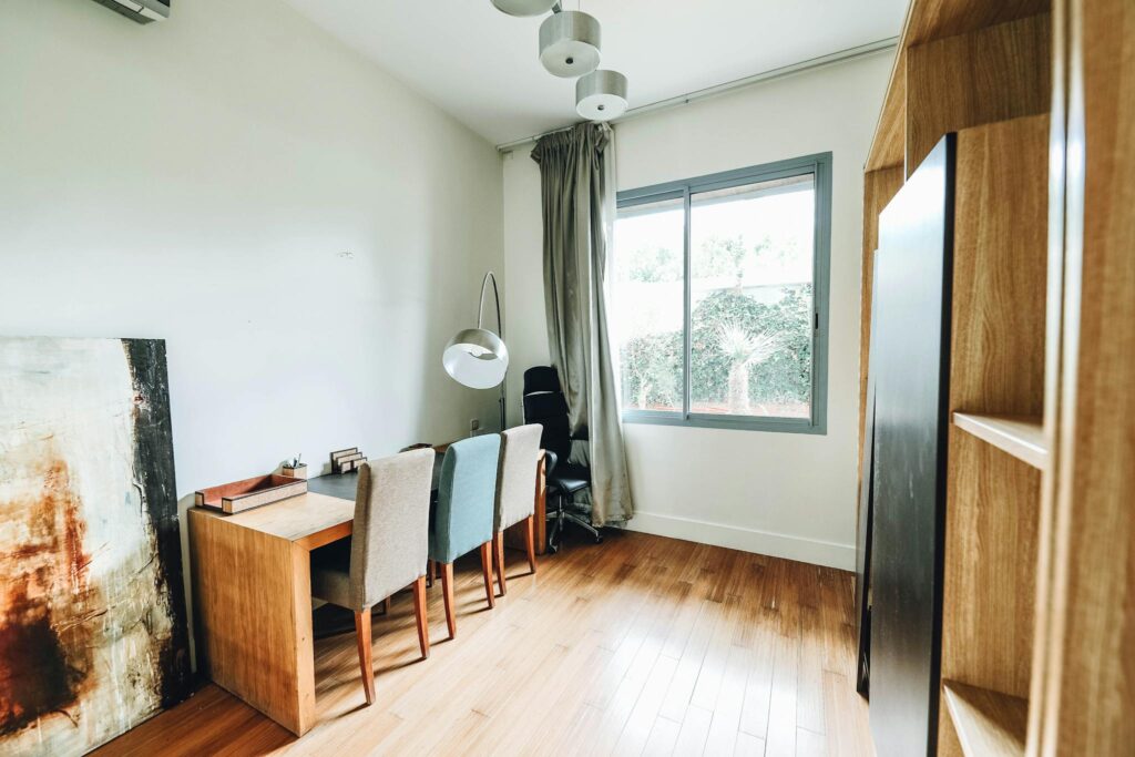 A modern, minimalist home office with clean lines, wooden floor, and ample natural light.
