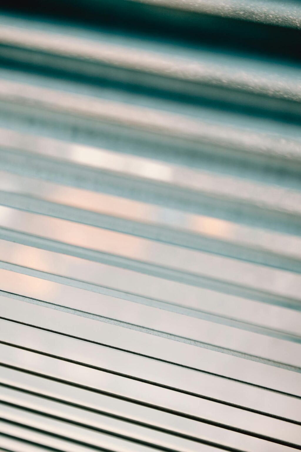 Closeup of half closed white metal blinds covering window in apartment during day