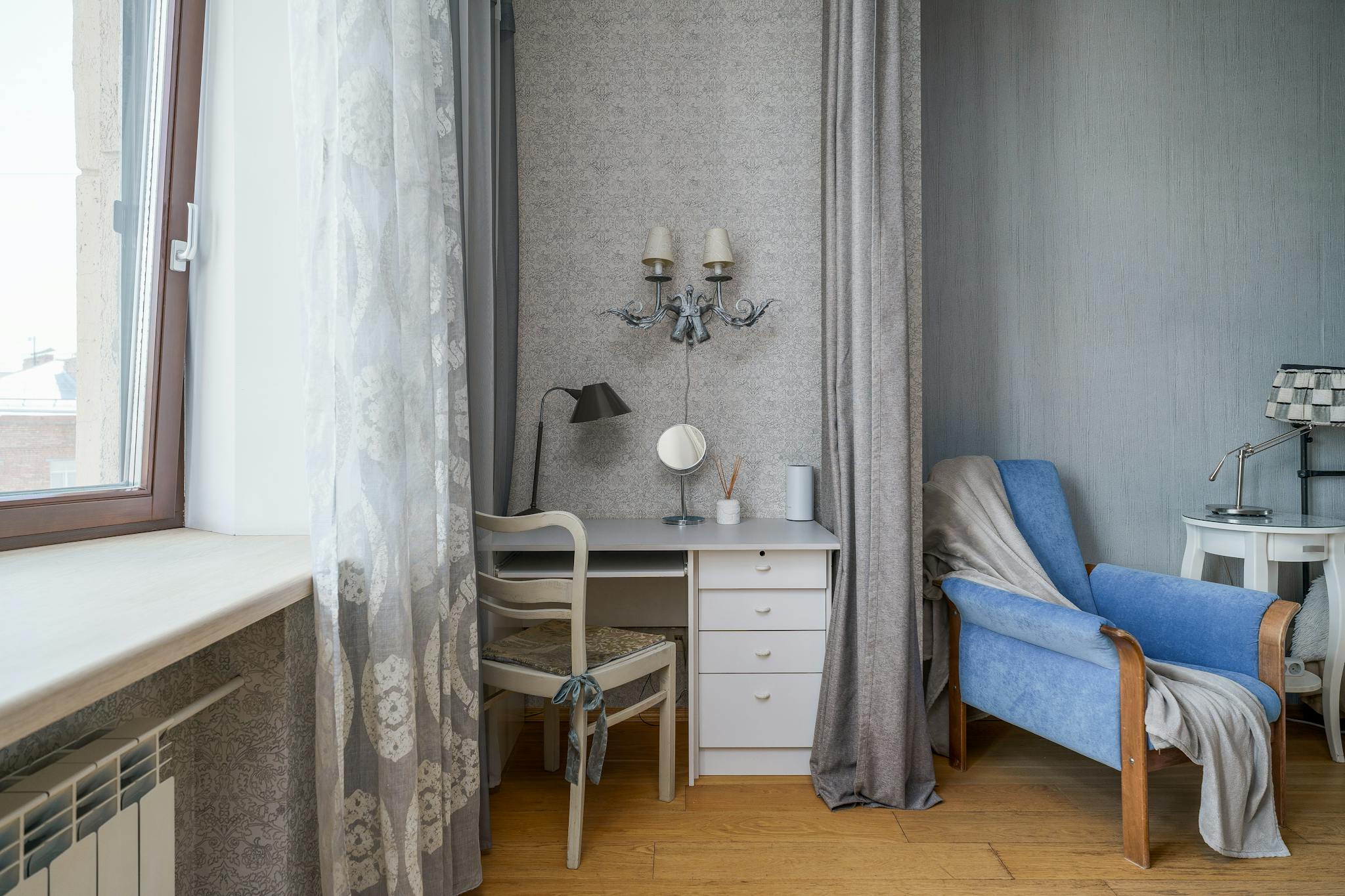 Elegant interior featuring a blue armchair, desk, and soft curtains, perfect for home decor inspiration.